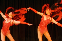 Two showgirls in red costumes and black and red feather headpiece